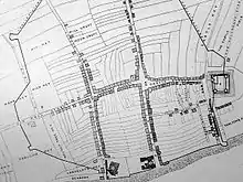 A black and white map, showing a town with a central street, criss-crossed by two adjoining small roads and a small castle on the far right of the map.